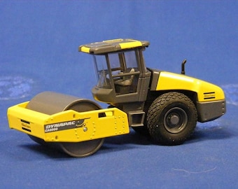 以下が含まれることがあります： 黄色と灰色のダイナパック CA3000 アスファルトローラーの玩具モデル。モデルは詳細なキャビンと大きなローラードラムを備えています。