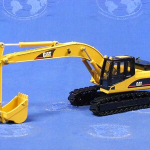Puede incluir: Modelo de juguete de excavadora Caterpillar 325D amarilla con orugas negras y una cabina negra. La excavadora tiene un brazo y una cuchara amarillos.