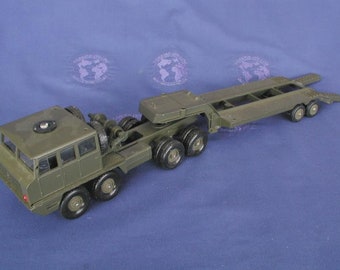 May include: A die-cast olive green military truck and trailer toy. The truck has a cab with windows and a flatbed trailer with multiple axles and wheels. The toy is designed to resemble a heavy-duty vehicle.