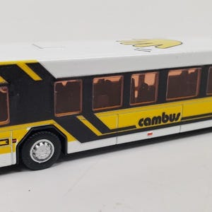 Peut inclure: Un bus jouet blanc et jaune avec des accents noirs. Le bus porte les mots "cambus" et "The University of Iowa" imprimés sur le côté. Le bus porte le numéro "111" imprimé sur le côté.