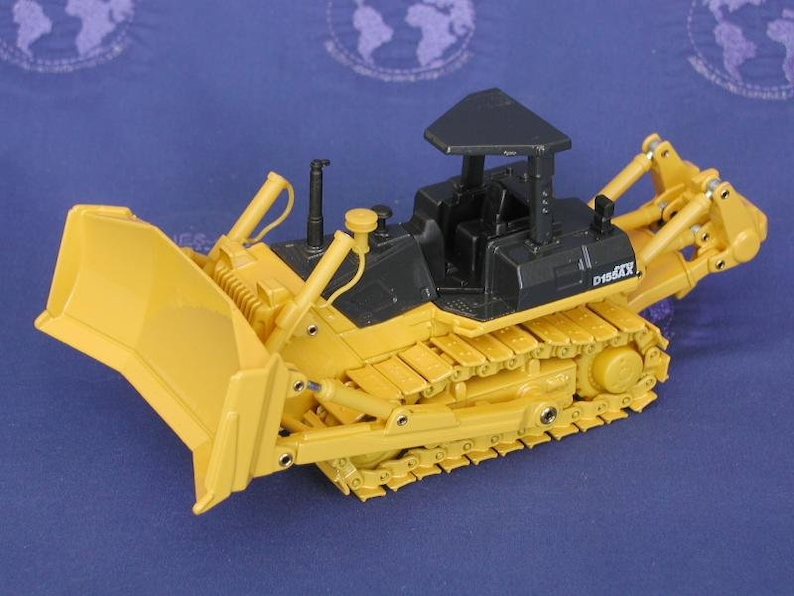 K&ouml;nnte beinhalten: Ein gelber und schwarzer Spielzeugbulldozer mit einer schwarzen Kabine und einer gelben Schaufel. Der Bulldozer hat ein D155XX-Schild an der Seite.