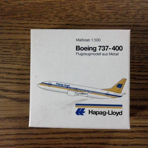 May include: A white box with a yellow and blue airplane model on it. The box says "Boeing 737-400" and "Hapag-Lloyd" on it.