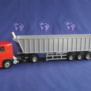 Puede incluir: Un camión volquete de juguete rojo y plateado. El camión tiene una cabina roja y una caja volquete plateada. El camión tiene seis ruedas y está sobre una superficie azul. Es una réplica en miniatura.