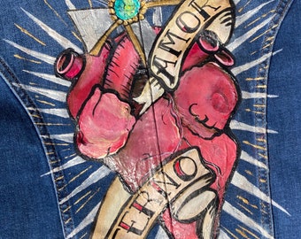 Puede incluir: Una chaqueta vaquera con un diseño pintado de un corazón, una cruz y dos rollos con las palabras "AMOR ETERNO" en letras doradas y negras.