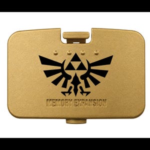 May include: A rectangular gold-colored plastic cover featuring a black printed emblem of a winged crest with a central triangle. The text "MEMORY EXPANSION" is embossed below the emblem, and four small circular indentations appear above it.
