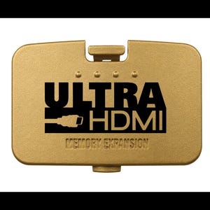 May include: A rectangular gold-colored plastic cover featuring the black printed text ULTRA HDMI and the words MEMORY EXPANSION below it. The cover includes a small connector tab at the top and bottom, with four small circular indentations above the text.