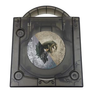 May include: A translucent dark gray plastic game console case with a top handle. The center features a circular graphic depicting a split image of a wolf and a human character, with a small gold Triforce emblem positioned between them.