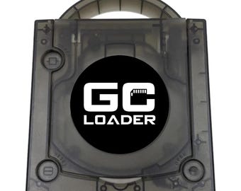 May include: A translucent dark gray square electronic device case with a handle on top. The center features a circular black emblem with the white text GC LOADER. The case includes circular buttons labeled POWER, RESET, and OPEN on the corners.