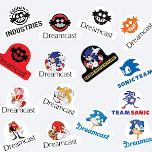May include: A collection of colorful stickers featuring characters and logos from the Sonic the Hedgehog video game series. The stickers include images of Sonic, Tails, Knuckles, and Dr. Eggman, along with the Dreamcast logo and text like "SONIC ADVENTURE" and "TEAM SANIC."