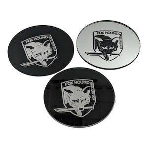 May include: Three round black and silver coasters with the words "FOX HOUND SPECIAL FORCE GROUP" and a stylized fox head with a knife in its mouth.