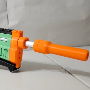 May include: A 3D-printed toy gun with a green and orange color scheme. The main body is green with the word "BOLT" printed on the side. An orange barrel extends from the front, and the design includes a silver tube.