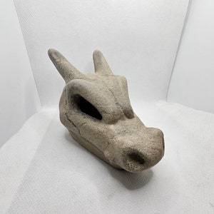 May include: A gray stone sculpture of a dragon head with a textured surface.