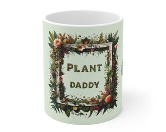 May include: White ceramic mug with a green background and a floral frame surrounding the text "PLANT DADDY".