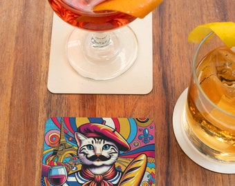 May include: A colourful coaster featuring a cartoon cat wearing a beret and a striped shirt, holding a glass of wine and a baguette. The background includes a stylised Eiffel Tower and other French-inspired designs.