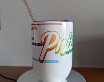 May include: White insulated tumbler with a rainbow "Pride" design. The tumbler has a silver straw and a clear lid. The design includes horizontal stripes and the word "Pride" in a colourful, cursive font. The tumbler sits on a reflective surface.