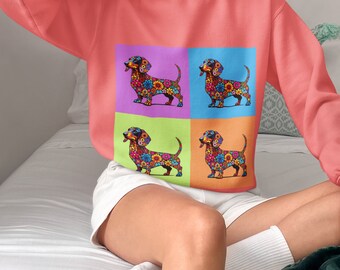 May include: A pink sweatshirt featuring a colourful dachshund design. The dachshund is made up of flowers and is repeated four times in a grid pattern.