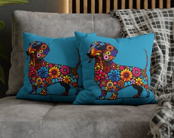 May include: Two blue cushion covers featuring a floral dachshund design. The dachshund is black with colourful flowers covering its body. The cushions are on a grey sofa.