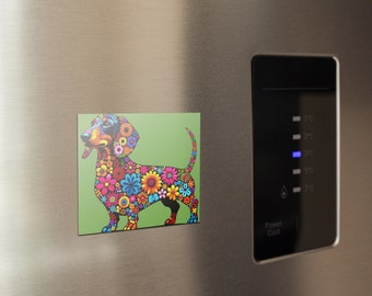 May include: A colourful dachshund magnet with a green background. The dachshund is made up of flowers in shades of pink, blue, yellow, orange, and green.