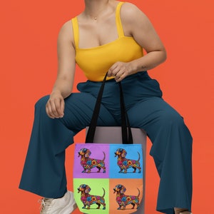 Könnte beinhalten: Eine Frau in einem gelben Tanktop und blauen Hosen sitzt auf einem Kasten und hält eine Tragetasche mit einem farbenfrohen floralen Dackel-Design. Die Tasche hat vier Paneele mit einem anderen Dackel auf jedem Paneel.