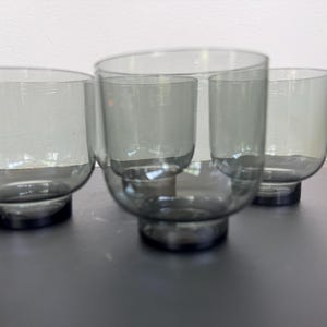 May include: Four gray-tinted glass tumblers with rounded bases. The glasses have a simple, modern design, perfect for serving beverages. The glasses are made of clear glass with a subtle gray hue.