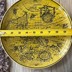 May include: Yellow decorative plate with a black world map design. The plate measures approximately 9 inches in diameter. The plate has a black rim and is on a wooden surface.
