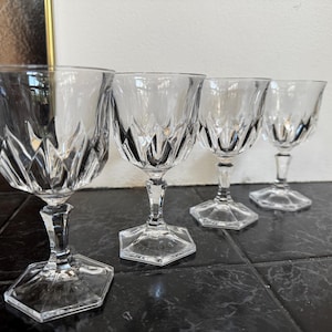 May include: Four clear crystal wine glasses with diamond-cut patterns on the bowls. The glasses have stems and hexagonal bases. The glasses are arranged in a row on a dark surface.