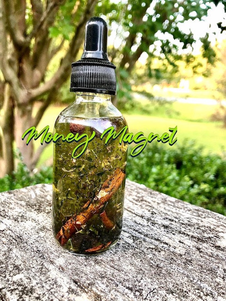 Pode incluir: Uma garrafa de vidro transparente com uma tampa conta-gotas preta, cheia de um l&iacute;quido verde e elementos bot&acirc;nicos. A garrafa tem as palavras "Money Magnet" em verde. A garrafa est&aacute; sobre uma superf&iacute;cie cinza desgastada.