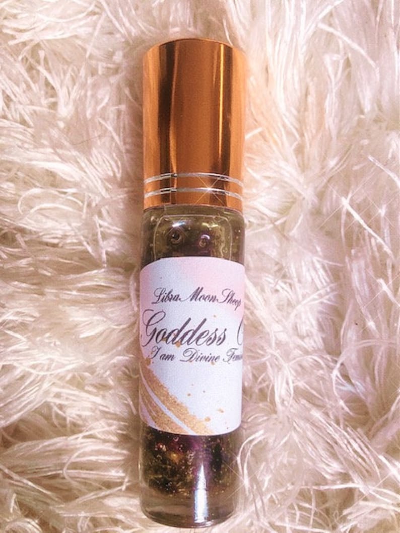 May include: A glass roller bottle with a gold cap and a white label. The label has black text that reads 'Liba Moon Shop Goddess Oil I am Divine Feminine'.