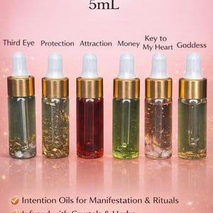May include: Six 5ml dropper bottles of sample oils, each with a different colour and contents. The bottles are labelled "Third Eye," "Protection," "Attraction," "Money," "Key to My Heart," and "Goddess." The text "Sample Oils" and "5mL" are at the top.