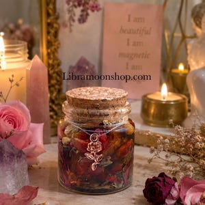 Puede incluir: Un frasco de vidrio transparente con tapón de corcho lleno de pétalos de flores y hierbas secas. Un colgante en forma de rosa cuelga de una cadena fina sobre el frente del frasco. El texto Libramoonshop.com es visible en una tarjeta rosa.