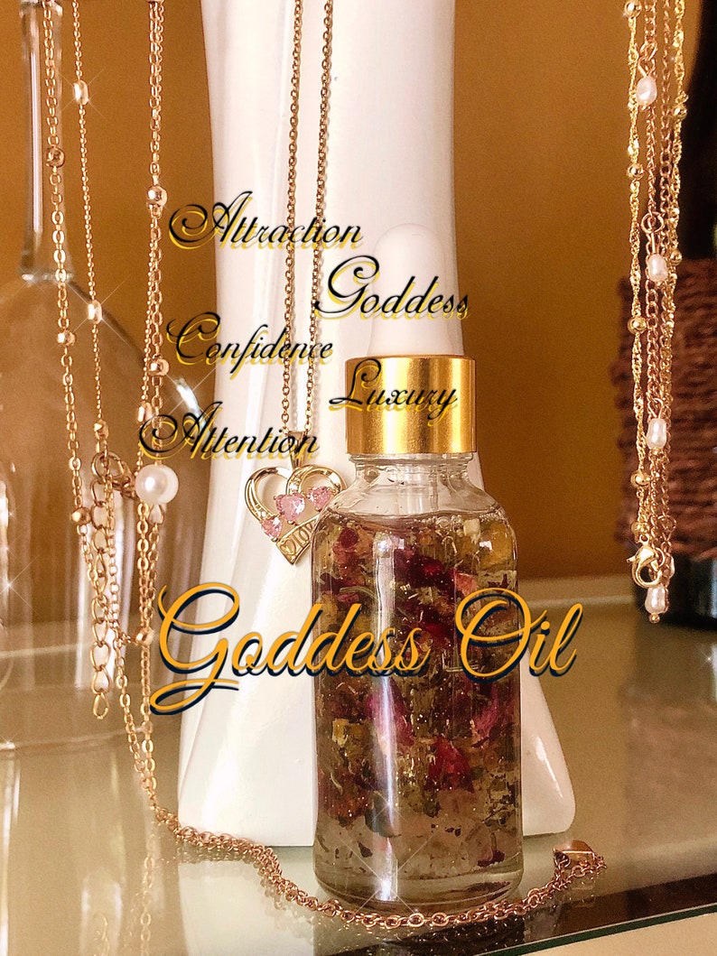 May include: A clear glass bottle of Goddess Oil with gold detailing and a gold cap, filled with dried flowers and herbs. Gold necklaces with charms and pearls hang around the bottle. The words "Attraction, Confidence, Attention, Goddess, Luxury, Goddess Oil" are written on the image.