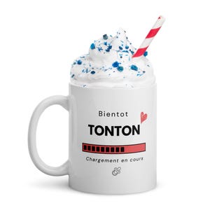 May include: White ceramic mug with the word "TONTON" in bold black letters, a red heart, and a loading bar graphic. The mug is topped with whipped cream, blue sprinkles, and a red and white striped straw.