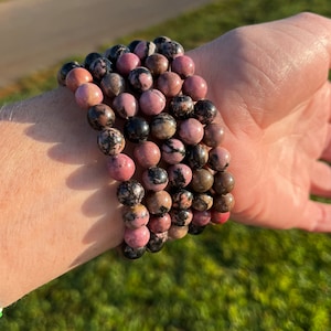May include: A stack of pink and black gemstone bracelets. The bracelets are made of round beads and are worn on a person's wrist.