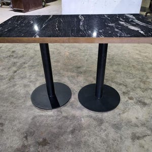 May include: A rectangular table with a black and white marble top and a bronze-coloured edge. The table is supported by two black, cylindrical legs with round bases. The table is designed for indoor use.