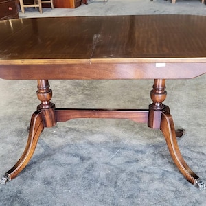 May include: Oval wooden dining table with a dark brown finish. The table has a double pedestal base with curved legs and decorative feet. The tabletop measures approximately 152 cm long.