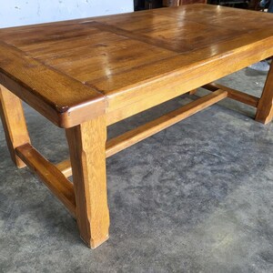 May include: A rectangular wooden coffee table in a medium-brown hue. The table has a paneled top and angled legs, connected by a stretcher. The wood grain is visible, giving it a rustic appearance. The table's dimensions are approximately 120 cm long.