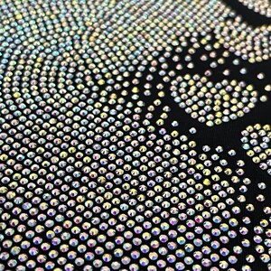 May include: A black fabric background covered in iridescent rhinestones forming a skull design.
