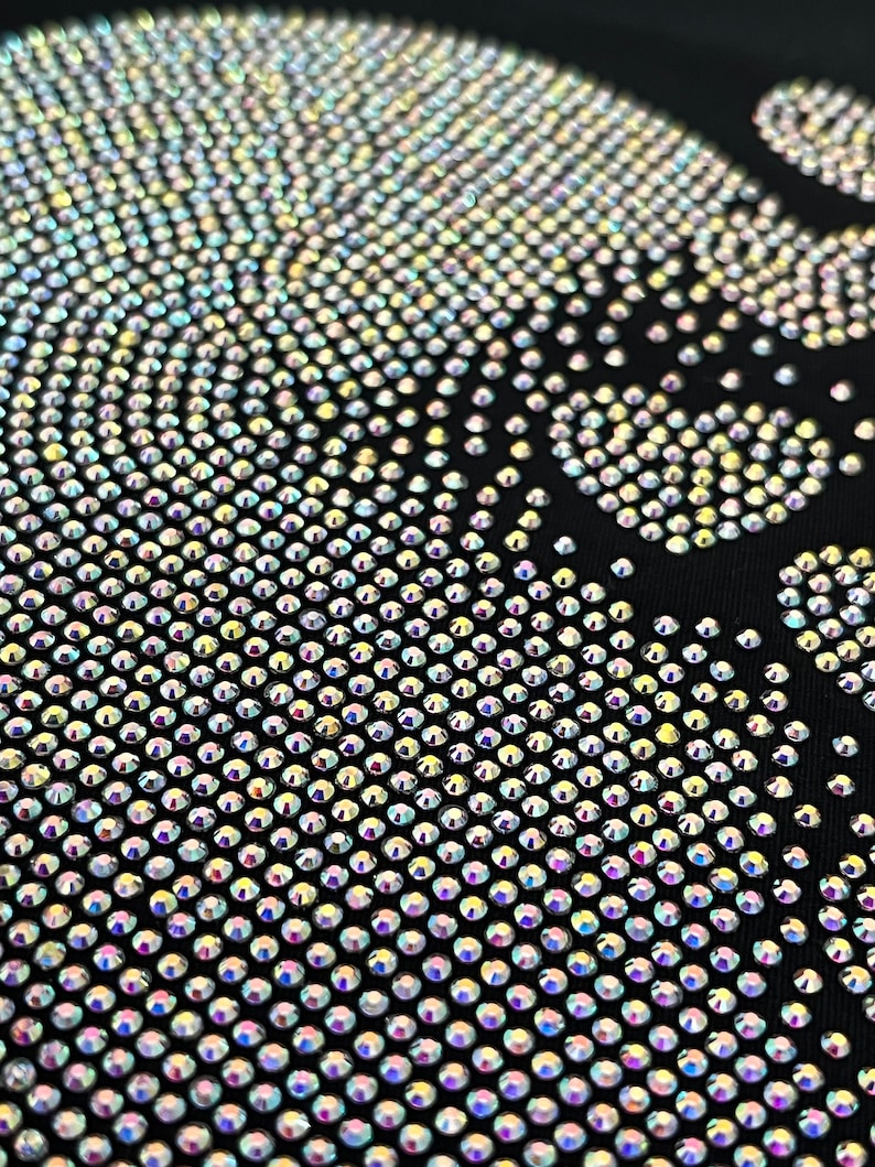May include: A black fabric background covered in iridescent rhinestones forming a skull design.