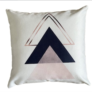 May include: White throw pillow with a geometric design featuring a navy blue triangle, a pink triangle, and a rose gold outline.