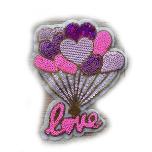 May include: A sequined patch featuring a bouquet of heart-shaped balloons in shades of pink and purple. The word "love" is spelled out in pink sequins at the bottom. The patch has a gold trim and is on a white background.