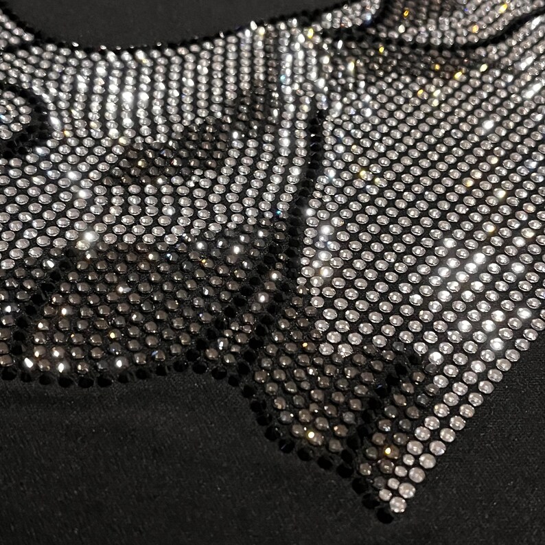 Op de afbeelding: Zwarte stof met een ontwerp van zilveren en zwarte strass in een geometrisch patroon.