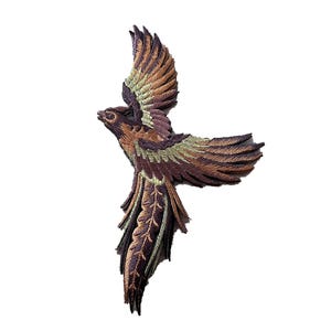 以下が含まれることがあります： 長い尾を持つ茶色と緑の刺繍された鳥のパッチ。鳥は羽を広げて飛行しています。