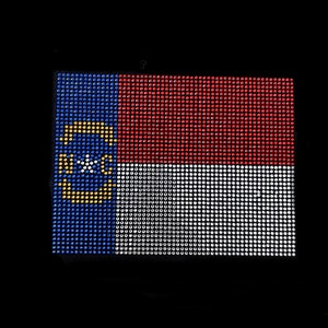Może przedstawiać: Flaga stanu Karolina Północna wykonana z cyrkonii. Flaga jest niebieska, biała i czerwona z żółtą gwiazdą w środku niebieskiego obszaru.