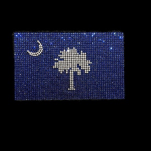 May include: A blue and white South Carolina state flag made of rhinestones. The flag features a crescent moon and a palmetto tree.