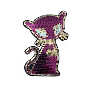 Puede incluir: Una aplicación de gato de lentejuelas rosa y dorada con contorno negro. El gato tiene ojos grandes azules y una nariz dorada.