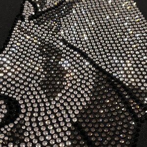 Op de afbeelding: Close-up van een zwarte stof bedekt met een patroon van zilveren en zwarte strass.