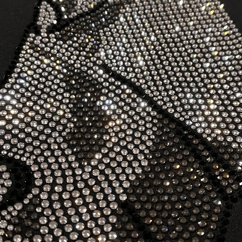 Op de afbeelding: Close-up van een zwarte stof bedekt met een patroon van zilveren en zwarte strass.