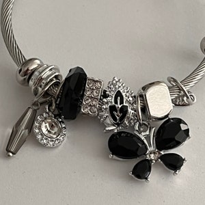 May include: A silver charm bracelet with black and clear crystal charms, including a butterfly charm with black crystal wings.