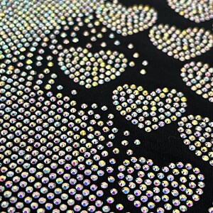 May include: A black fabric background with a skull design made of iridescent rhinestones.