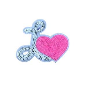 Puede incluir: Un parche de lentejuelas plateadas para planchar en forma de la letra "L" con un corazón rosa.